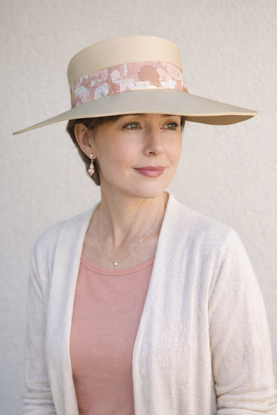 Woman wearing a wide-brimmed hat with floral band against a plain background