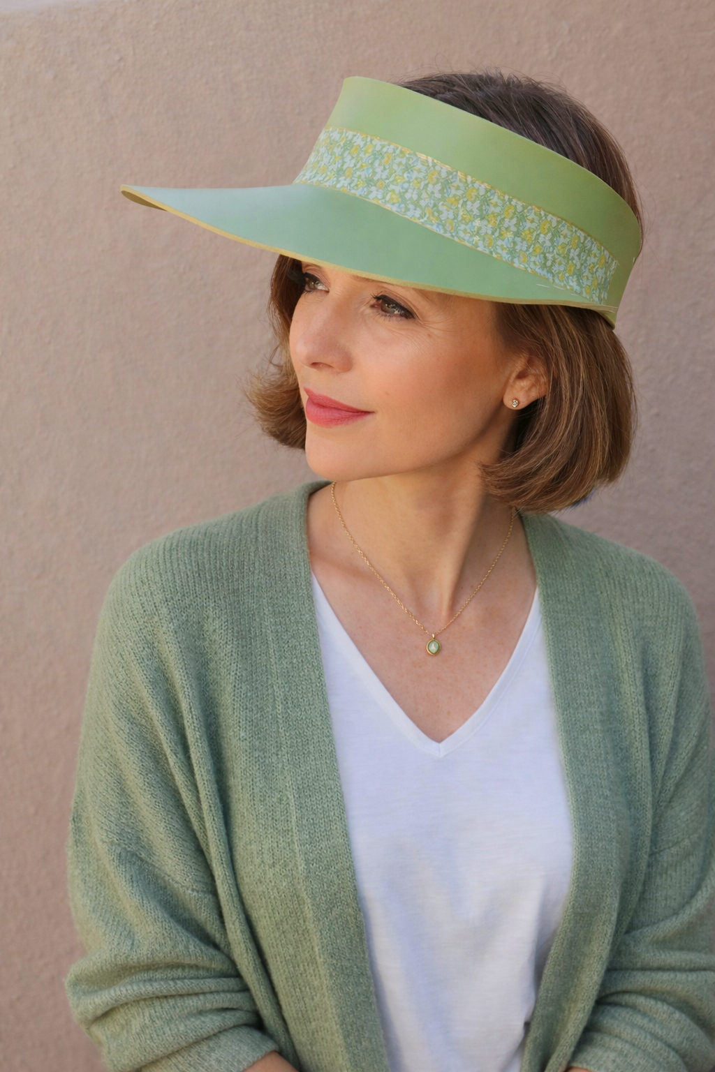 Woman wearing a green visor and cardigan against a beige background