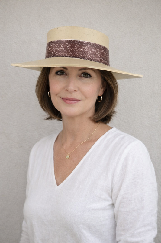 Woman wearing a wide-brimmed hat with a decorative band against a plain background
