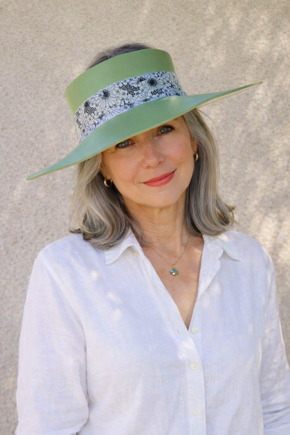 Woman wearing a green visor with floral band against a beige wall