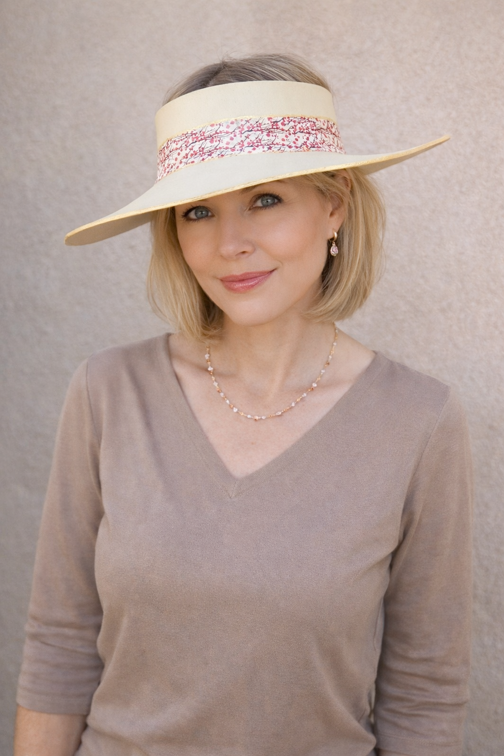 Woman wearing a beige visor with a pink band against a neutral background