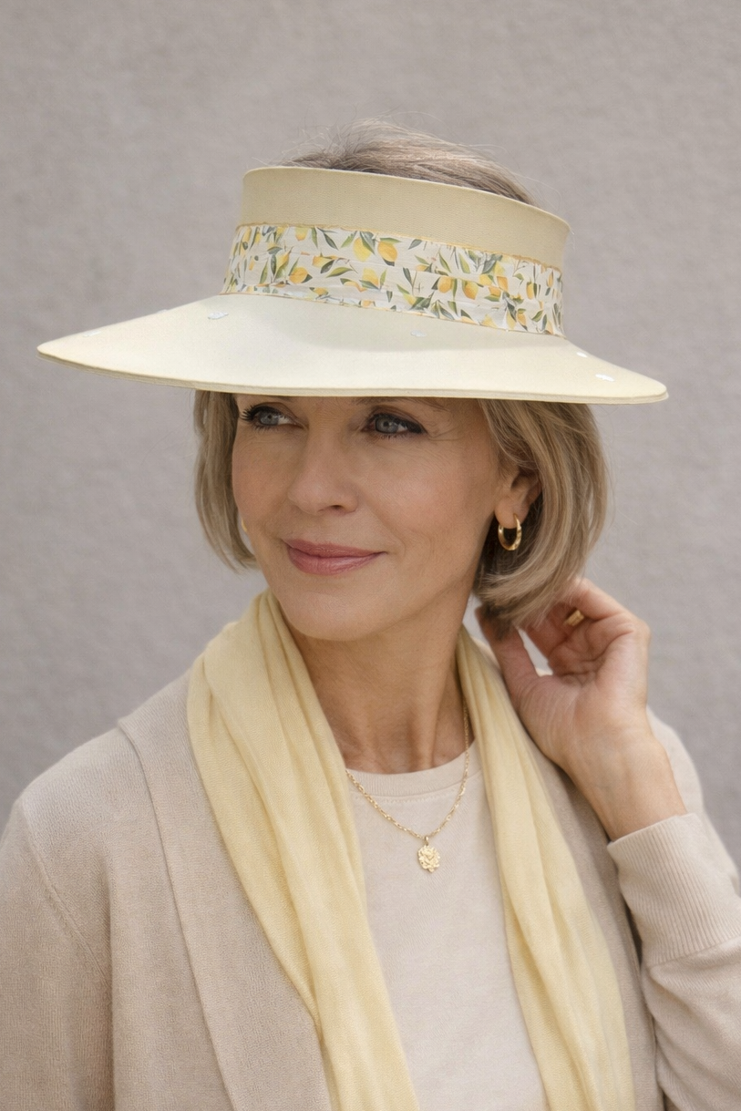 Woman wearing a wide-brimmed beige hat with floral embellishments against a plain background