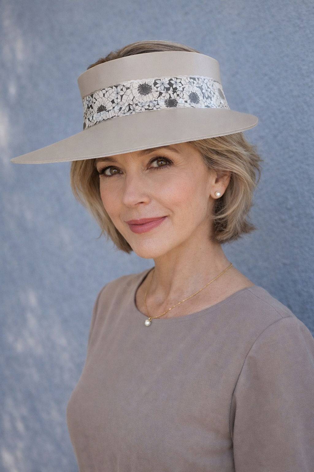 Woman wearing a beige hat with floral band against a textured blue background