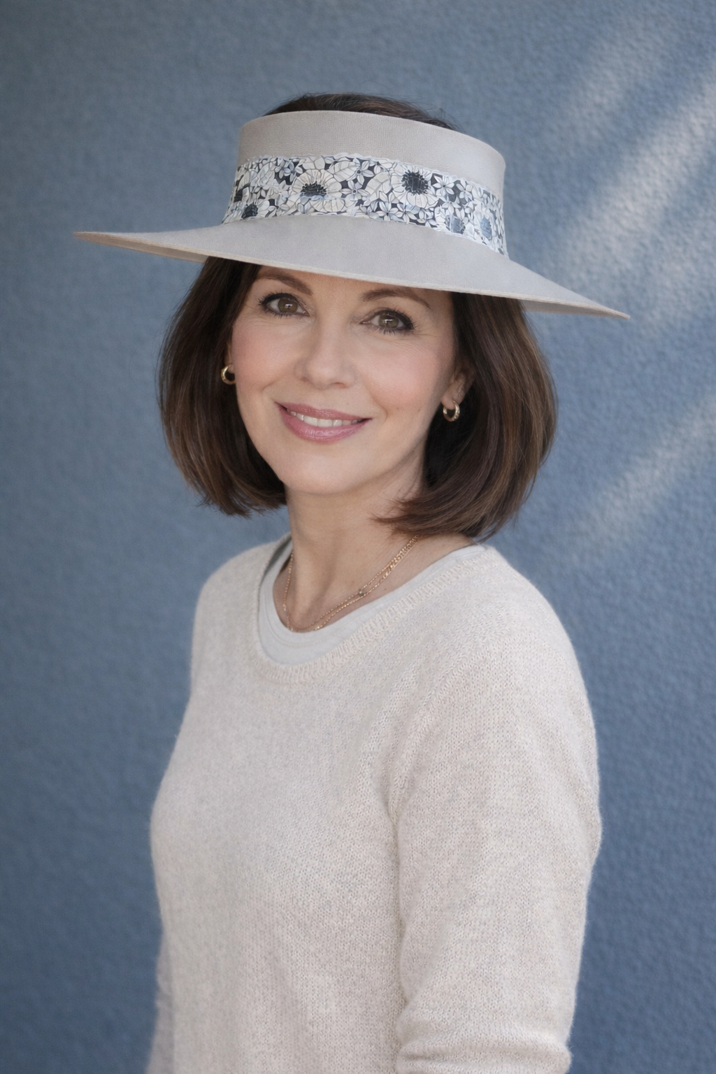 Woman wearing a wide-brimmed hat with floral embellishments against a blue background