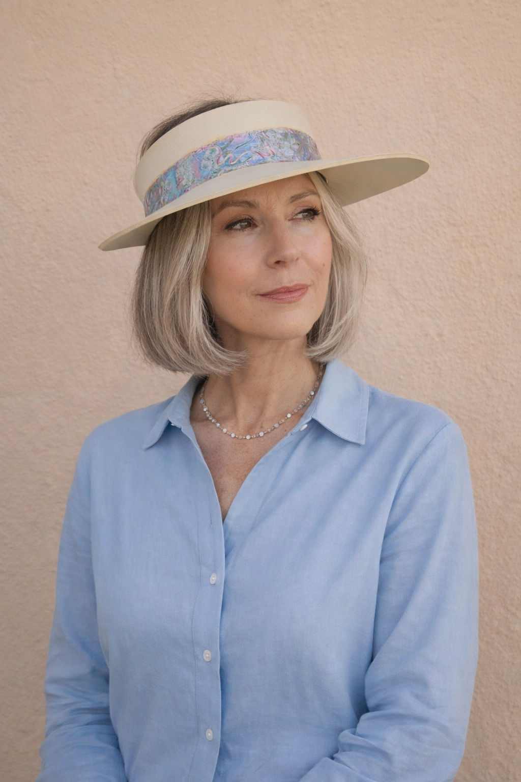 Woman wearing a light blue shirt and a wide-brimmed hat with a decorative band against a beige background