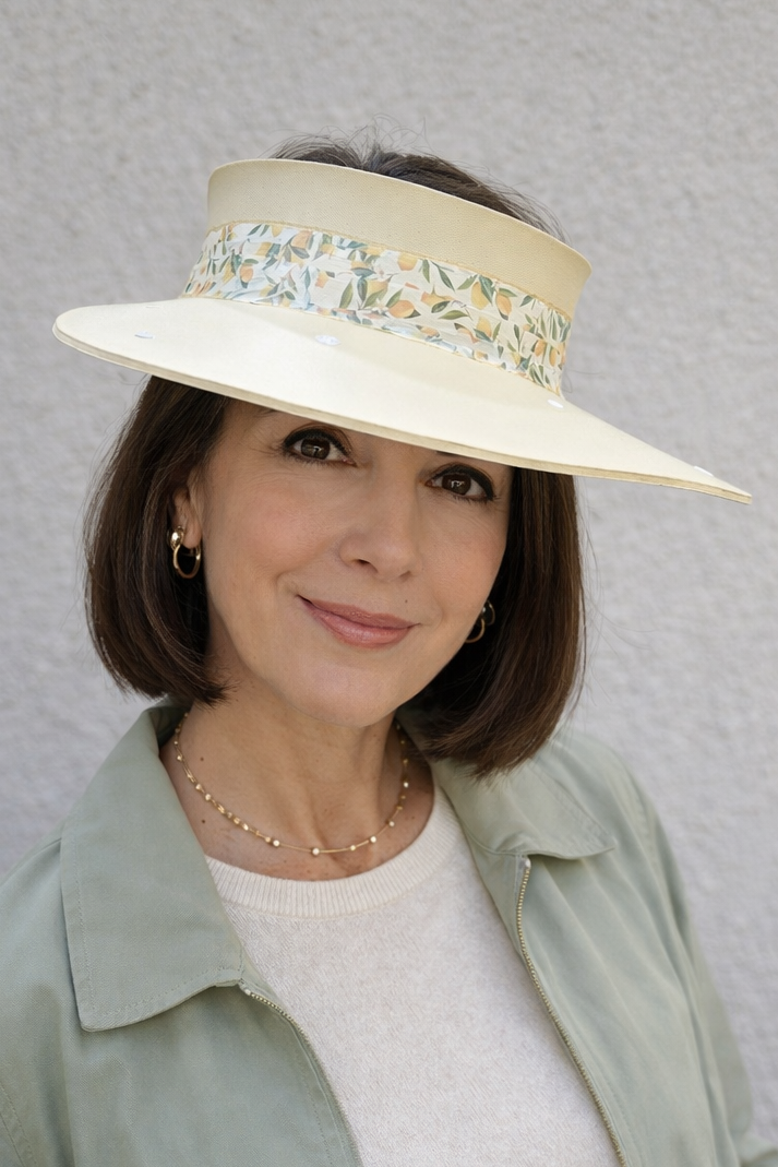 Woman wearing a wide-brimmed hat with floral embellishments against a gray background