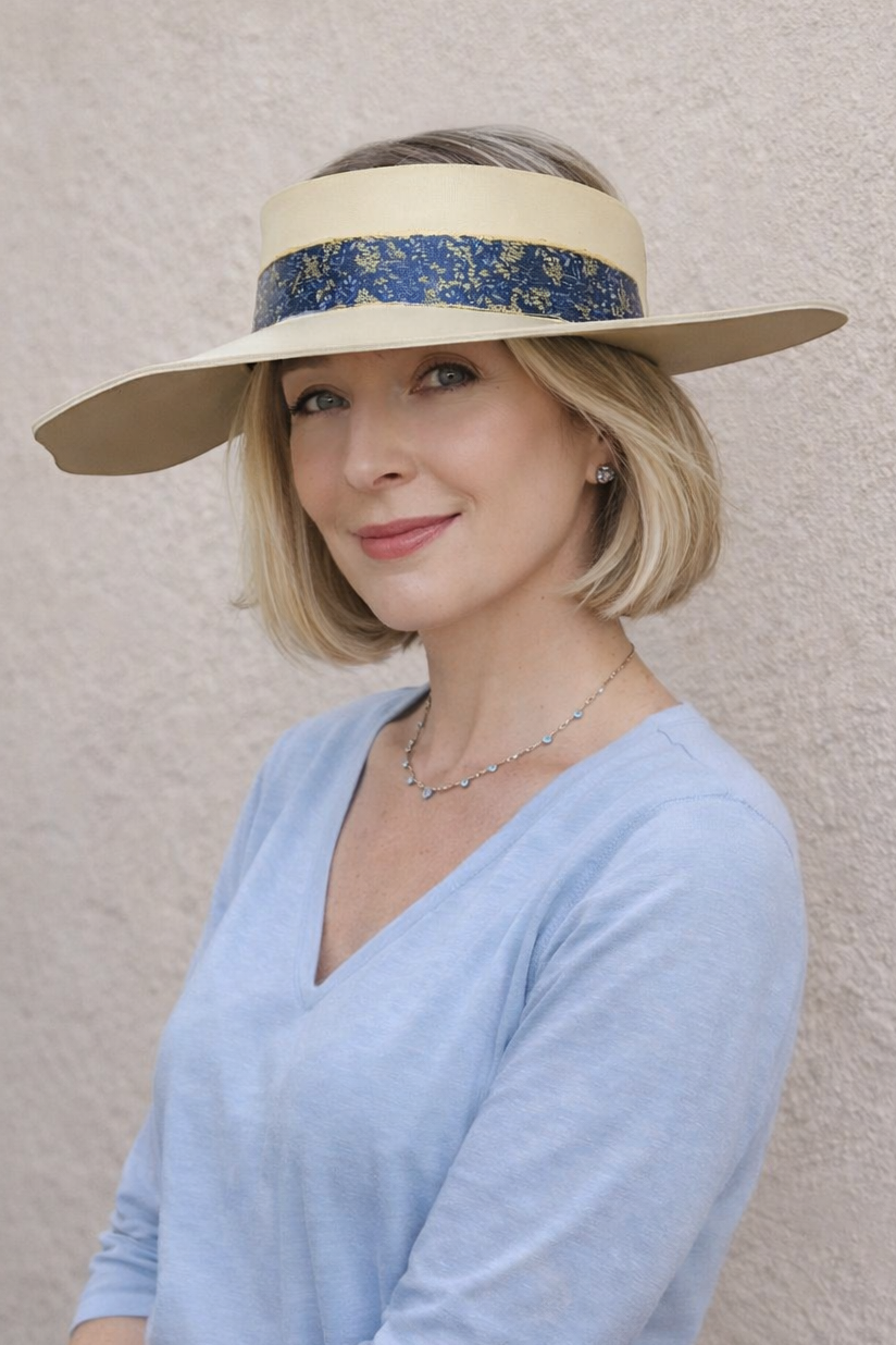 Woman wearing a light blue top and beige hat with a decorative band against a plain background