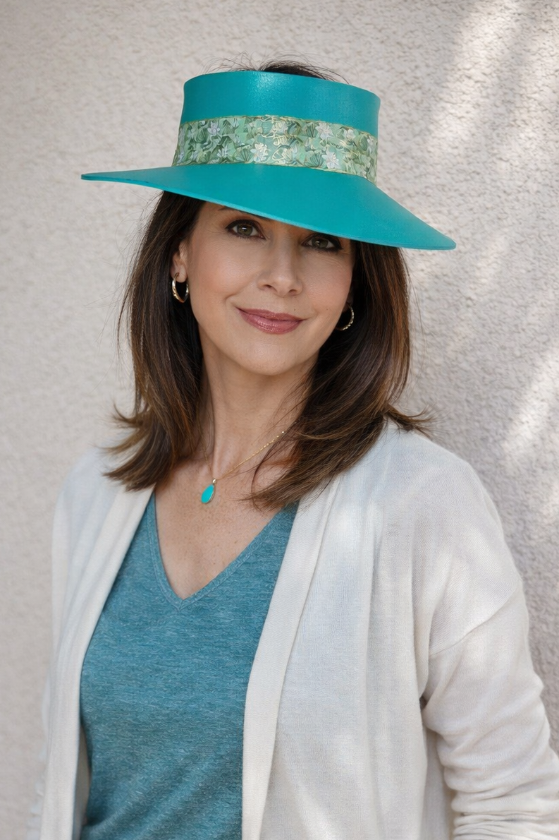 Woman wearing a turquoise visor hat and white cardigan against a neutral background