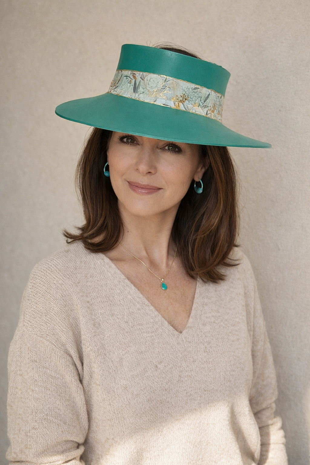 Woman wearing a teal hat with a patterned band against a plain background