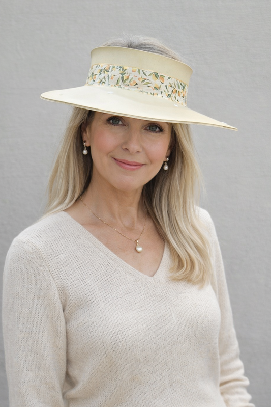 Woman wearing a beige hat with floral embellishments against a gray background