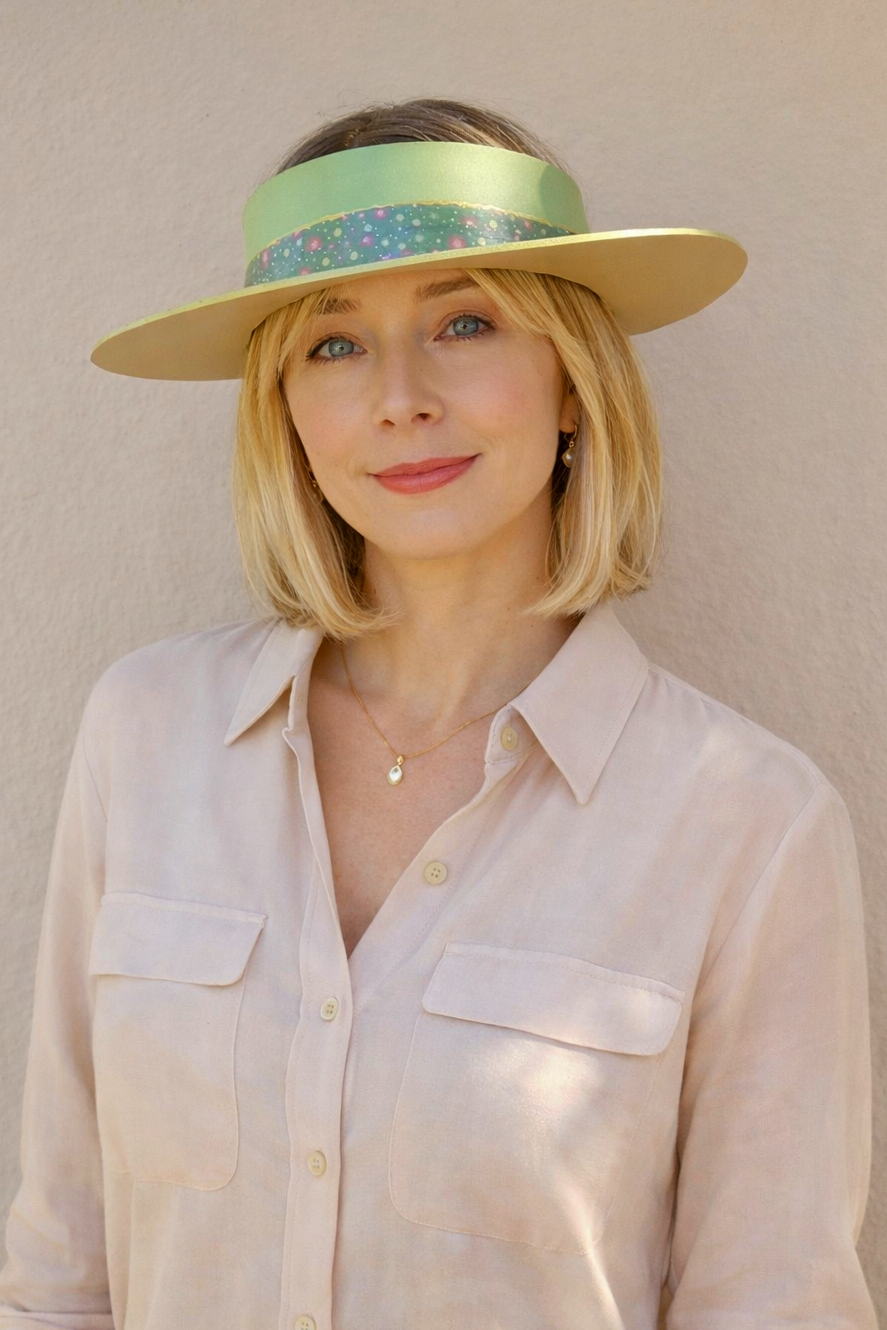 Woman wearing a light-colored shirt and a visor hat against a plain background