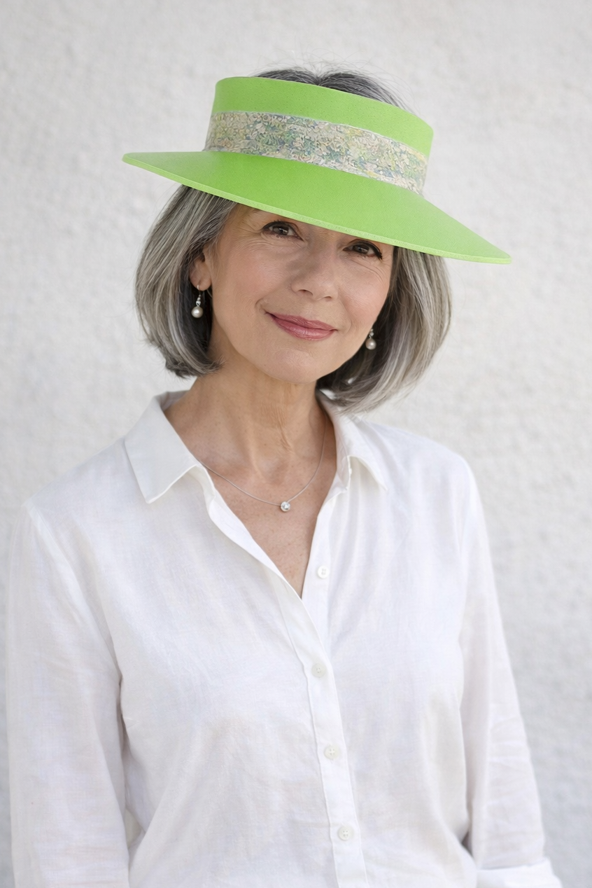 Woman wearing a bright green sun hat with a white shirt and light pants against a plain background