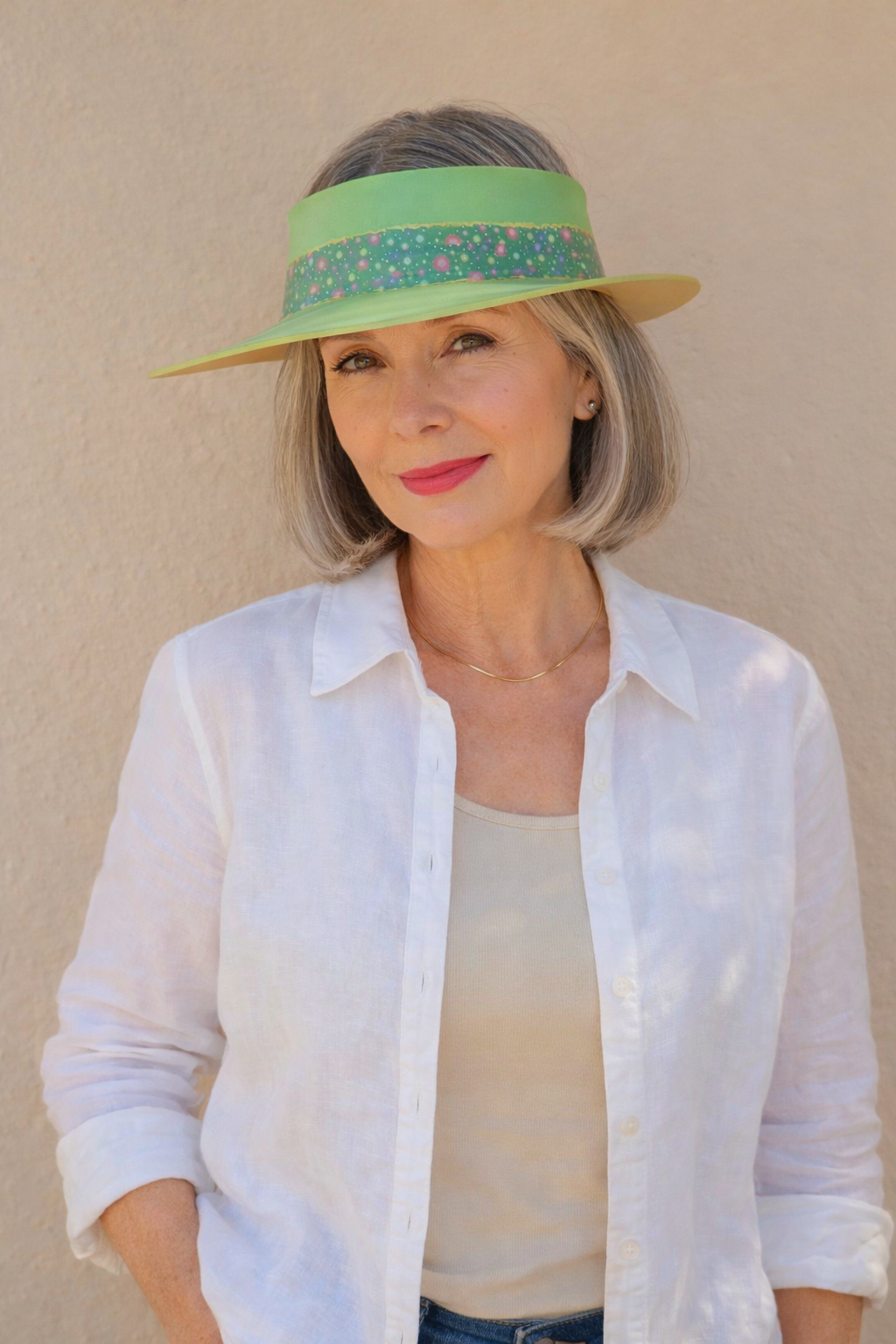 Woman wearing a white shirt and a green visor against a beige background