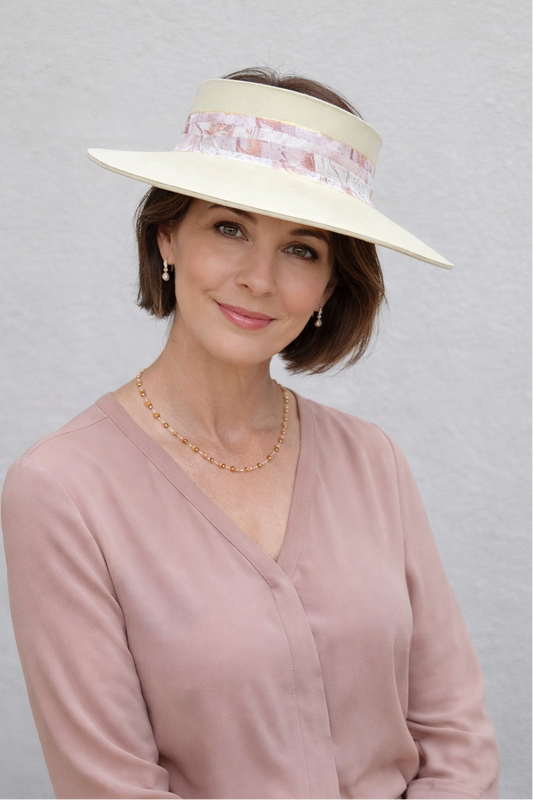 Woman wearing a light pink blouse and a white visor with decorative band against a gray background
