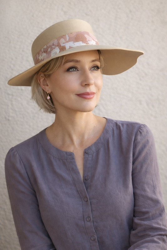 Woman wearing a beige hat with floral band against a plain background