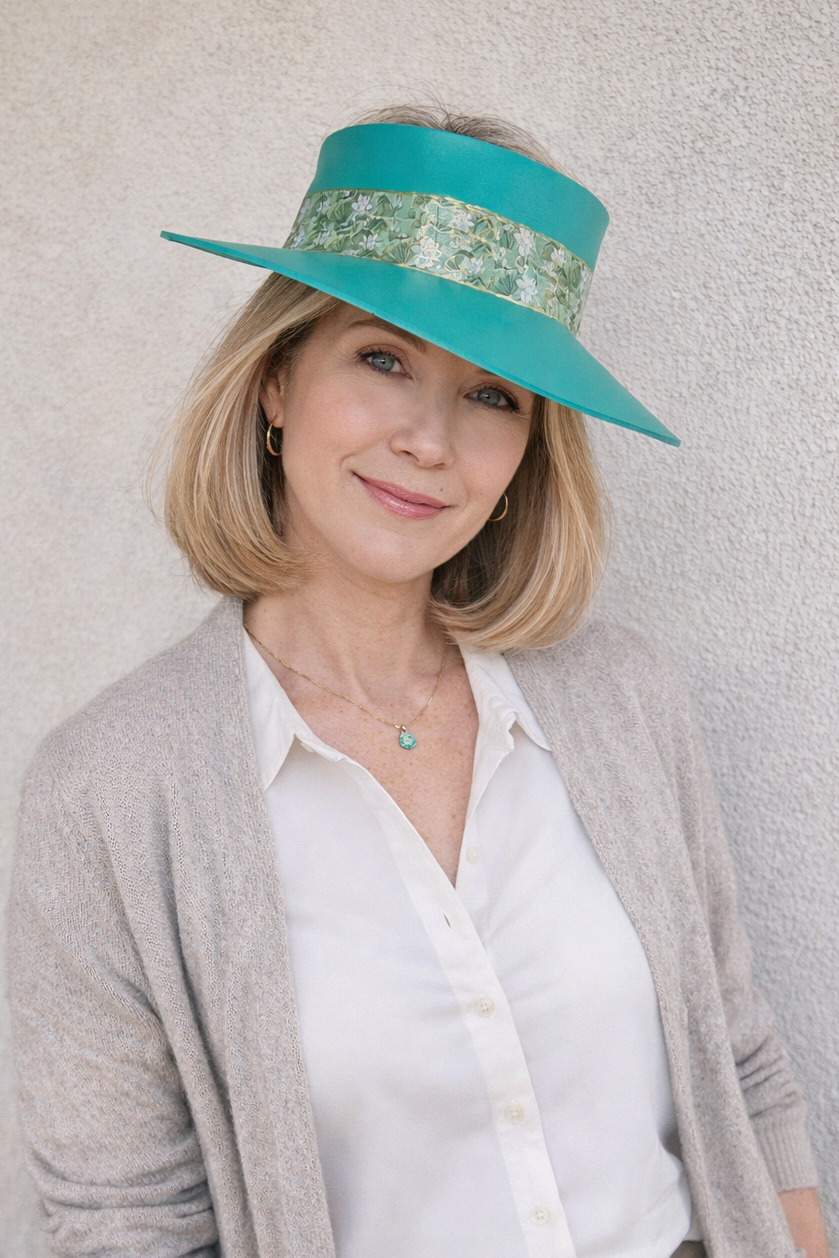 Woman wearing a teal sun hat with a patterned band against a plain background