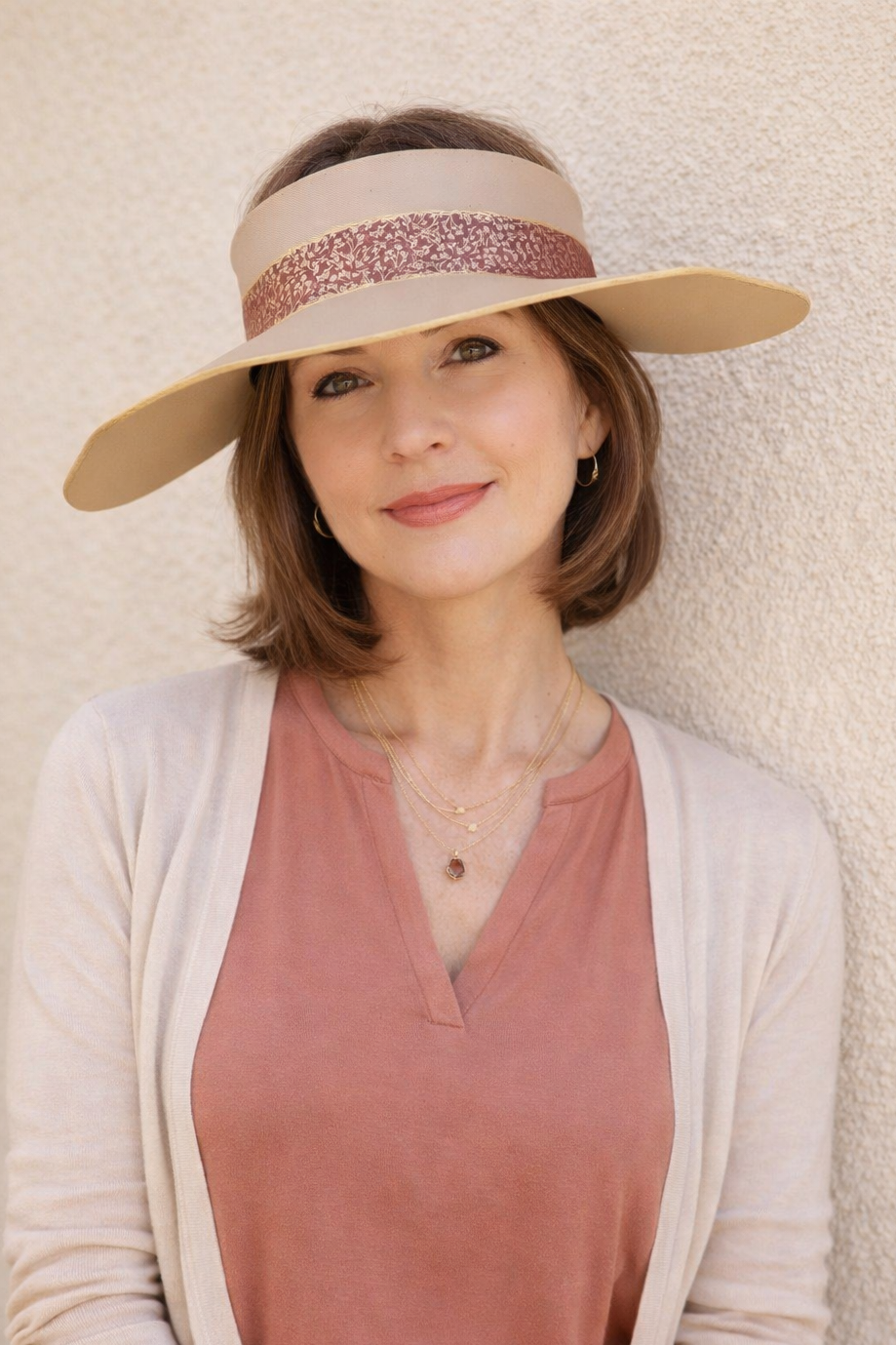 Woman wearing a beige visor and pink top against a light background