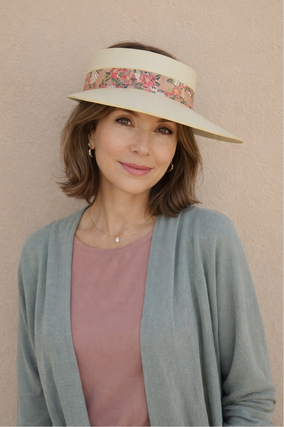 Woman wearing a wide-brimmed hat with a floral band against a beige background