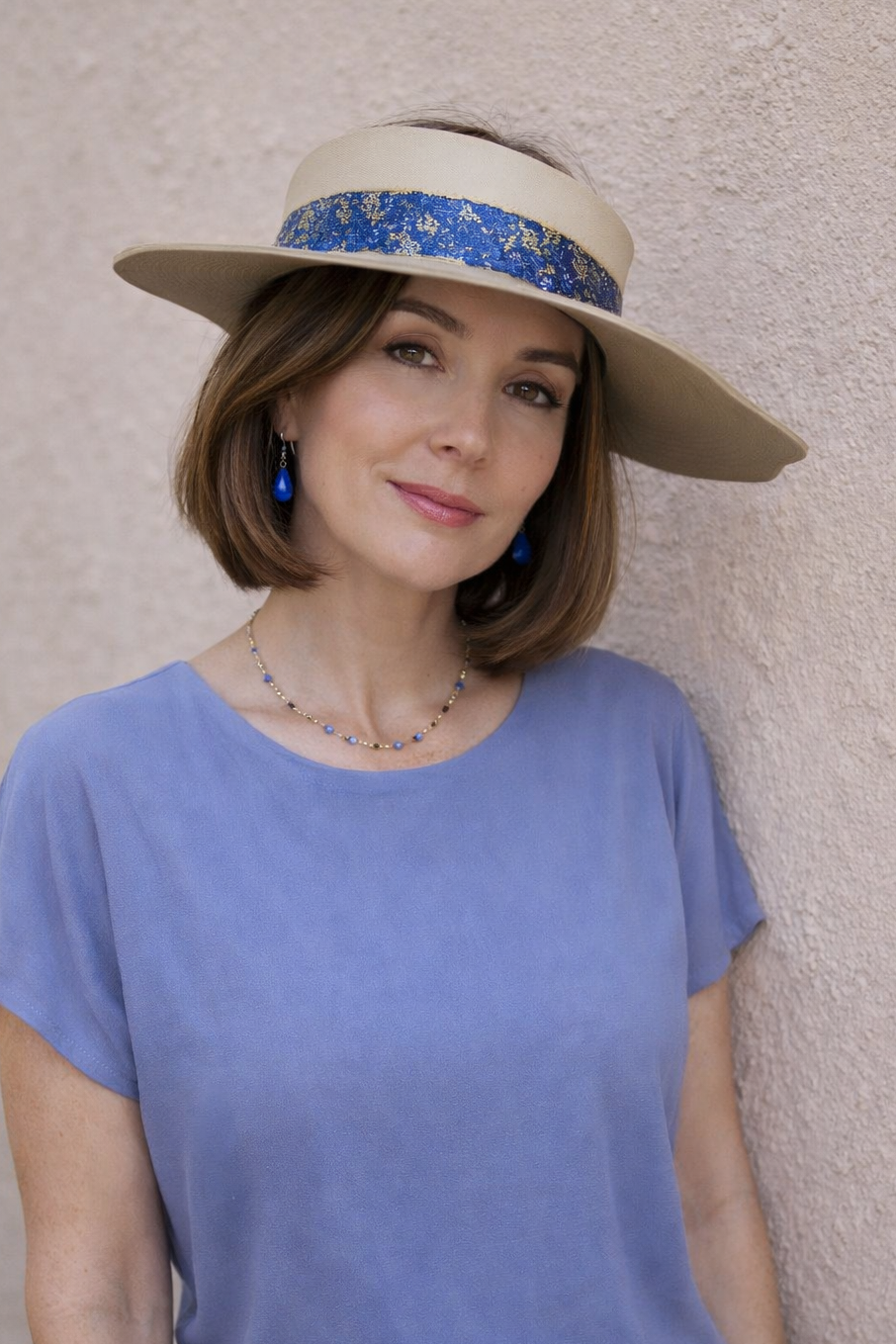 Woman wearing a wide-brimmed hat with a decorative band against a plain background