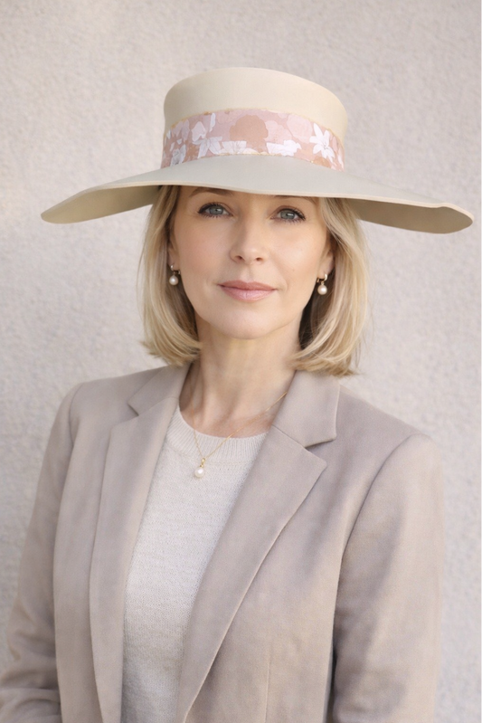 Woman wearing a wide-brimmed hat with floral details against a plain background