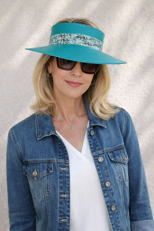 Woman wearing a turquoise visor, sunglasses, and denim jacket against a neutral background