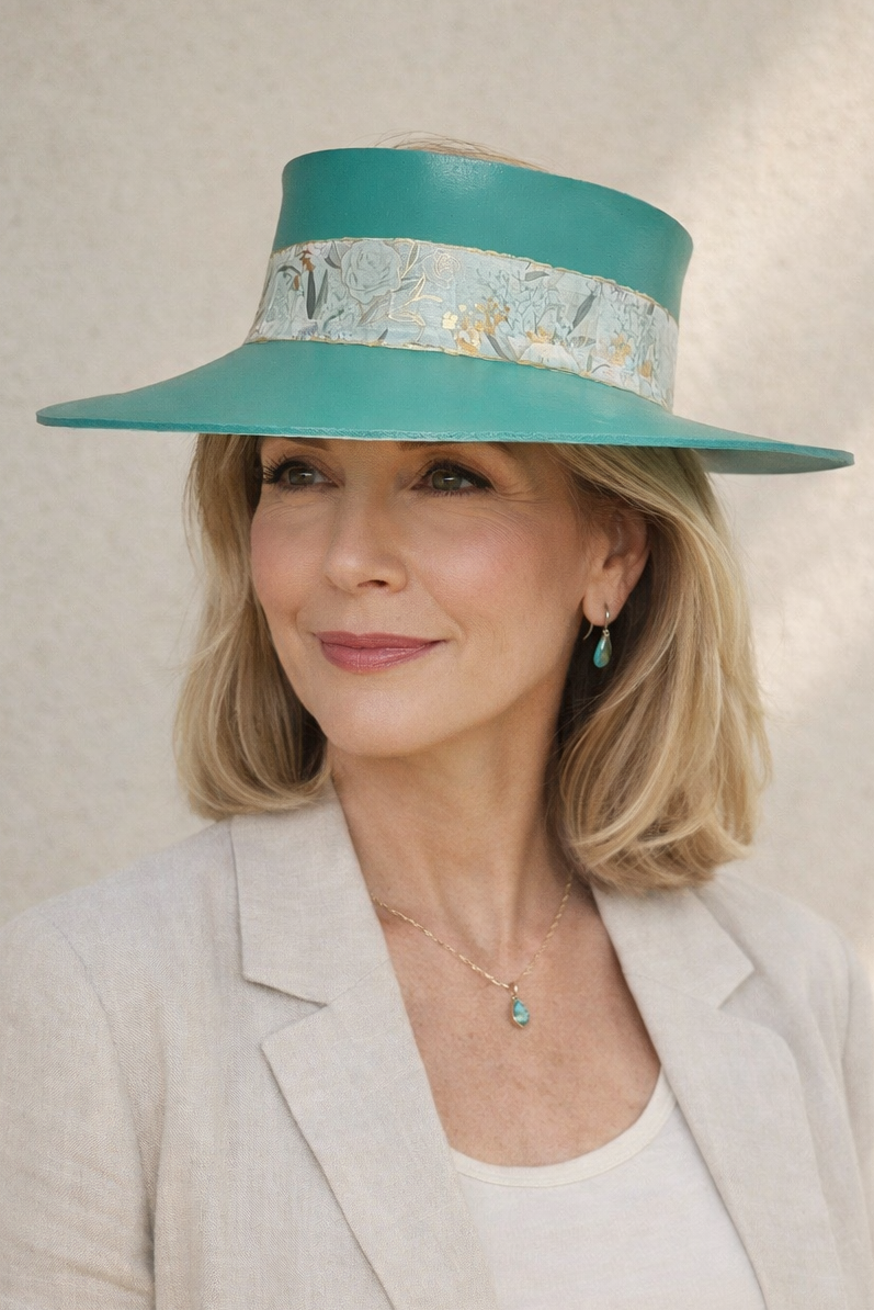 Woman wearing a teal hat with decorative band against a neutral background