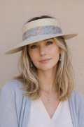 Woman wearing a wide-brimmed hat with floral band against a beige background