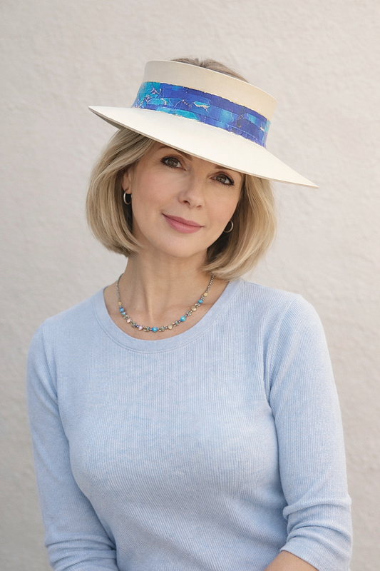 Woman wearing a light blue sweater and a decorative sun visor hat against a plain background