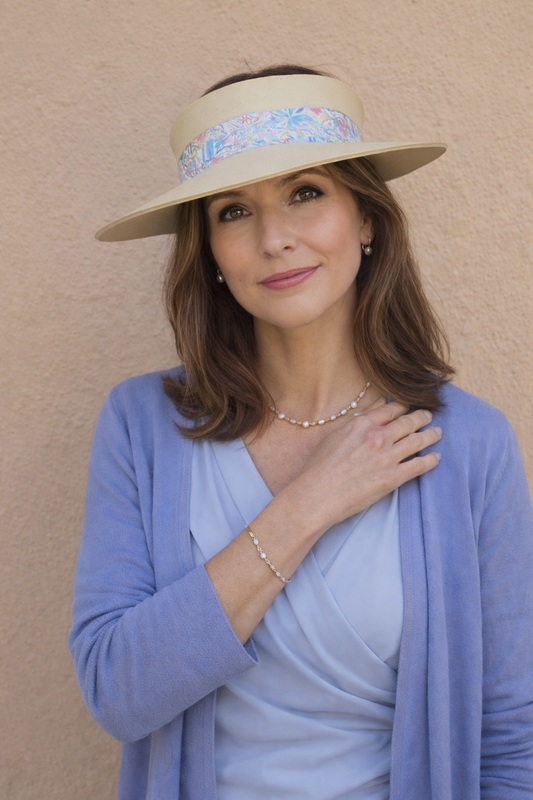 Woman wearing a wide-brimmed hat with a decorative band against a beige wall.