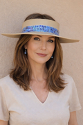 Woman wearing a wide-brimmed hat with a decorative band against a beige wall.