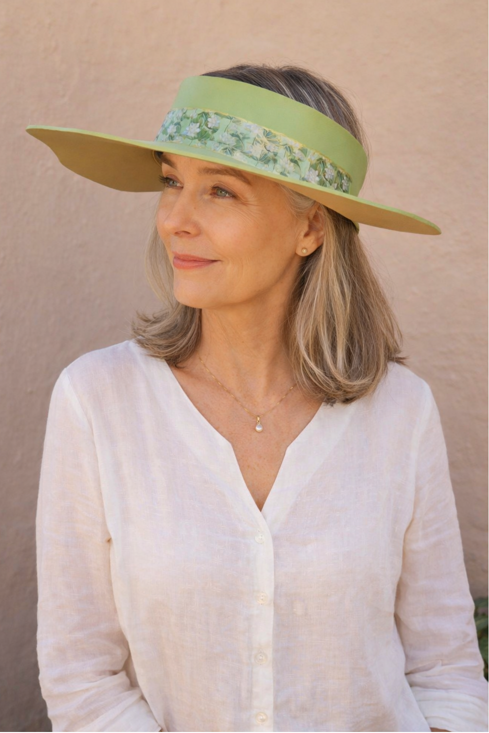 Woman wearing a wide-brimmed hat with floral band against a beige background