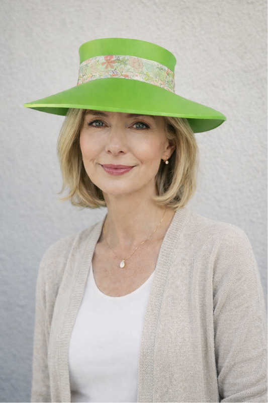 Woman wearing a bright green hat with floral band against a plain background