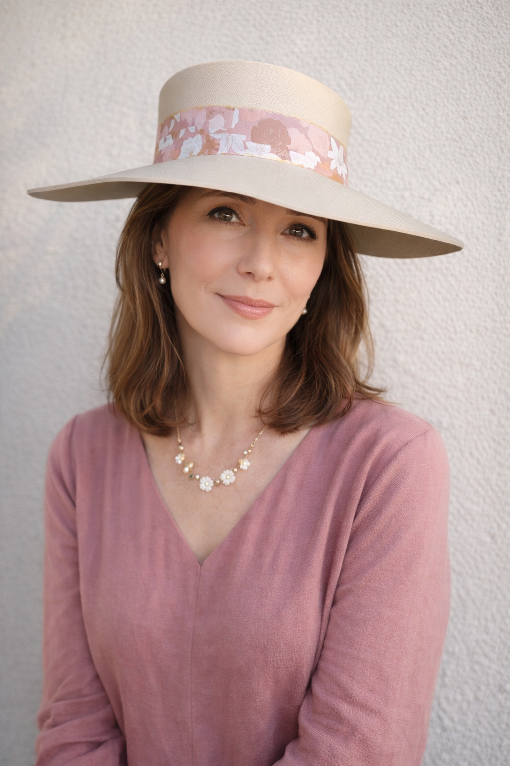Woman wearing a wide-brimmed hat with a floral band against a plain background