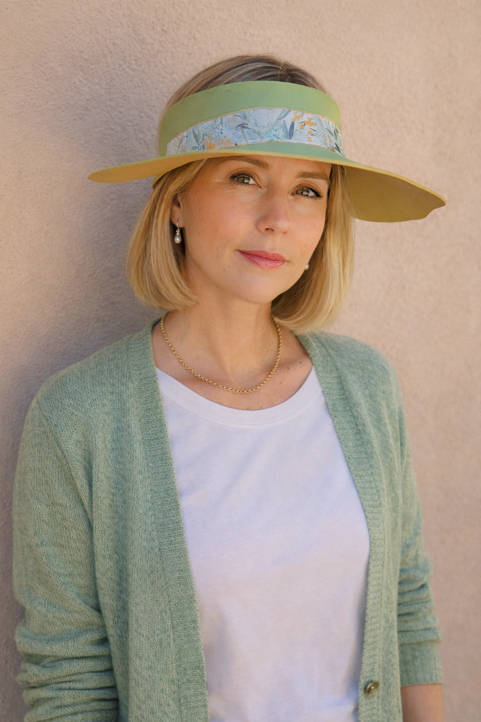 Woman wearing a green visor and light green cardigan against a beige wall
