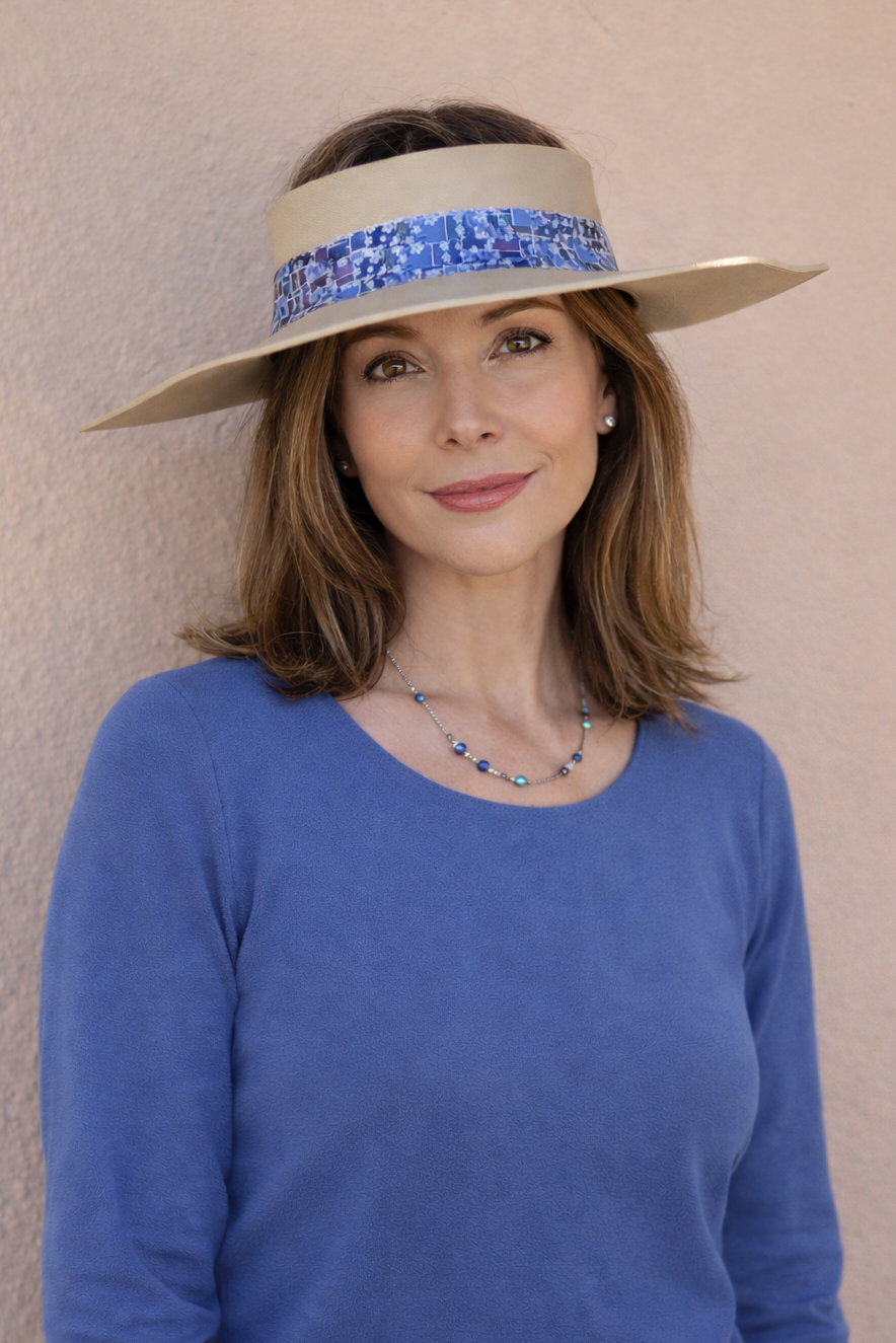 Woman wearing a wide-brimmed hat with a blue band against a beige wall
