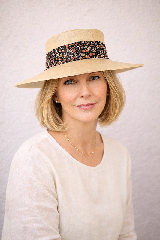 Woman wearing a wide-brimmed hat with a floral band against a plain background