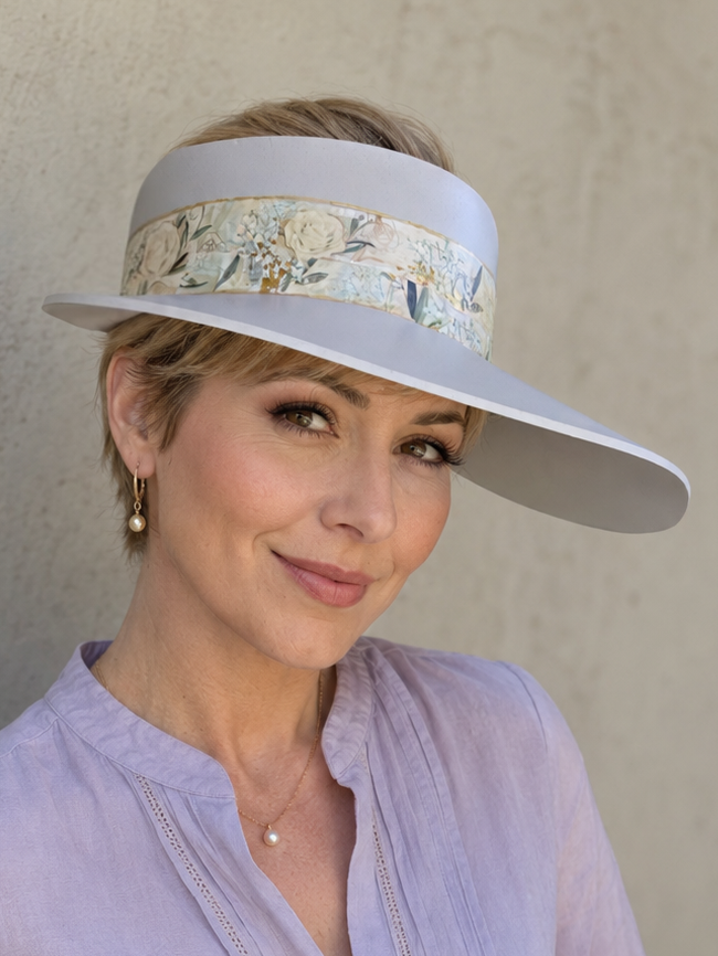 Woman wearing a light purple blouse and a wide-brimmed hat with a floral band against a plain background