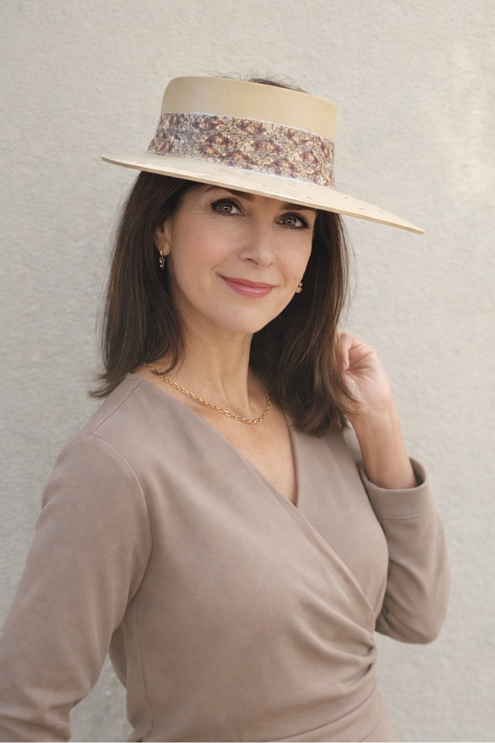 Woman wearing a beige hat with decorative band against a plain background