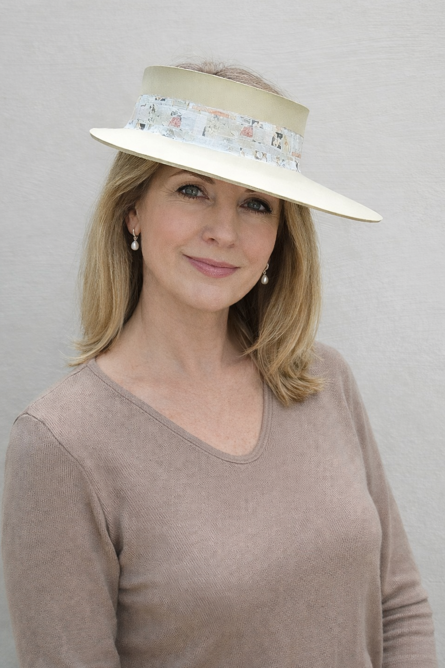 Woman wearing a beige hat with floral band against a plain background