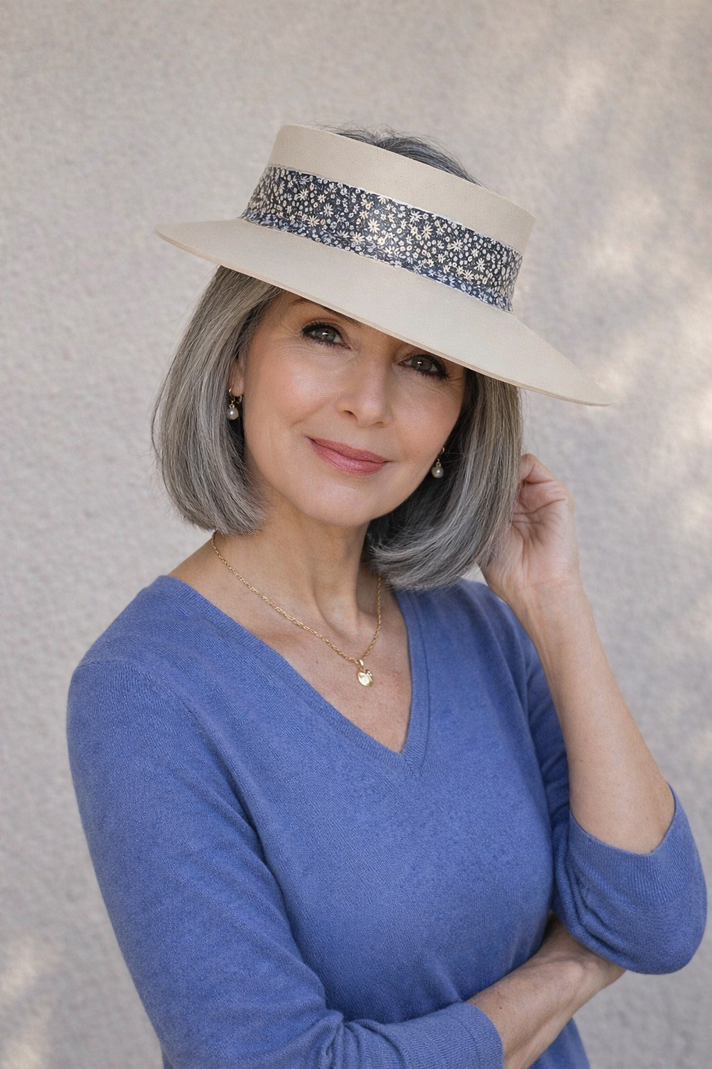Woman wearing a blue top and beige hat with a decorative band against a neutral background